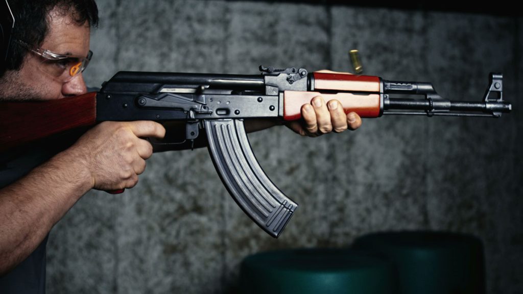 A man fires an AK-47 style rifle using a standard capacity magazine.