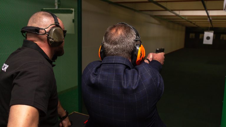 A man target shooting with an instructor behind him.